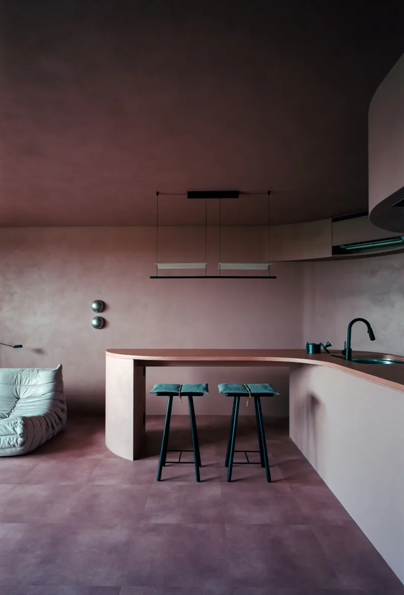 Open kitchen and dining area with pink toned plaster walls, curved island and black bar stools