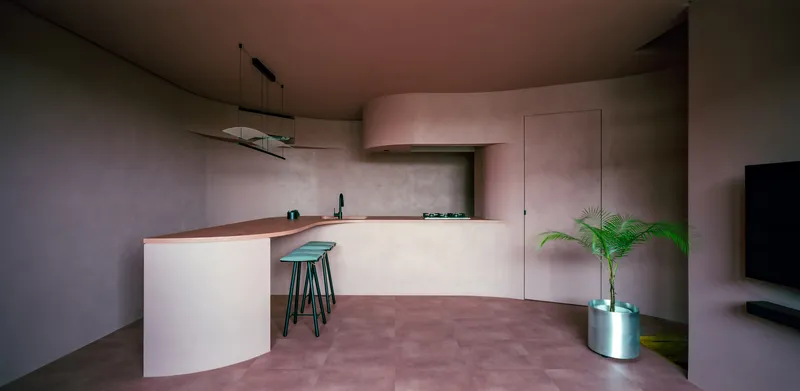 Wide view of the curved kitchen counter with a potted palm and pink polished concrete floor