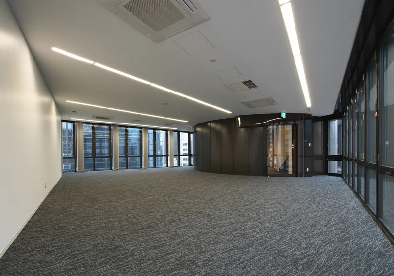 Open office floor with grey carpet, linear recessed lighting, and continuous glazing along the perimeter