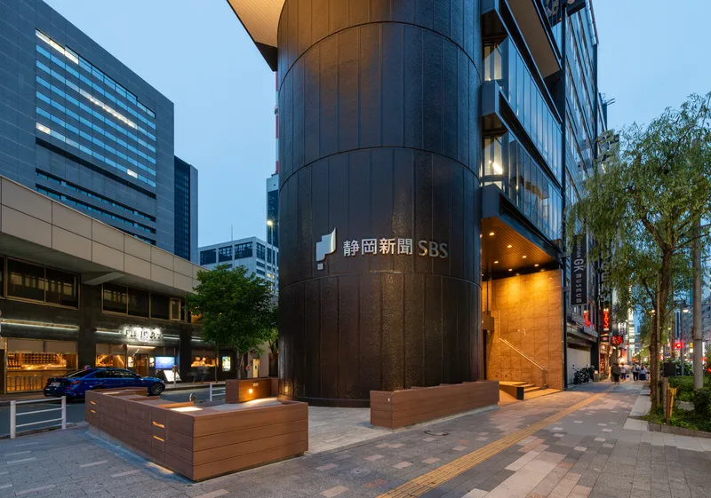 Street-level view of the curved bronze-paneled column and timber benches at twilight