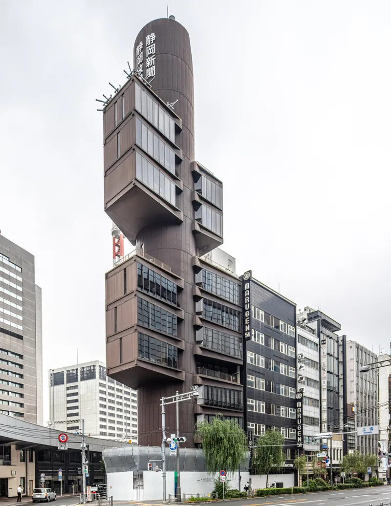Street-level view of the stacked cantilevered volumes wrapping the cylindrical central shaft under overcast skies