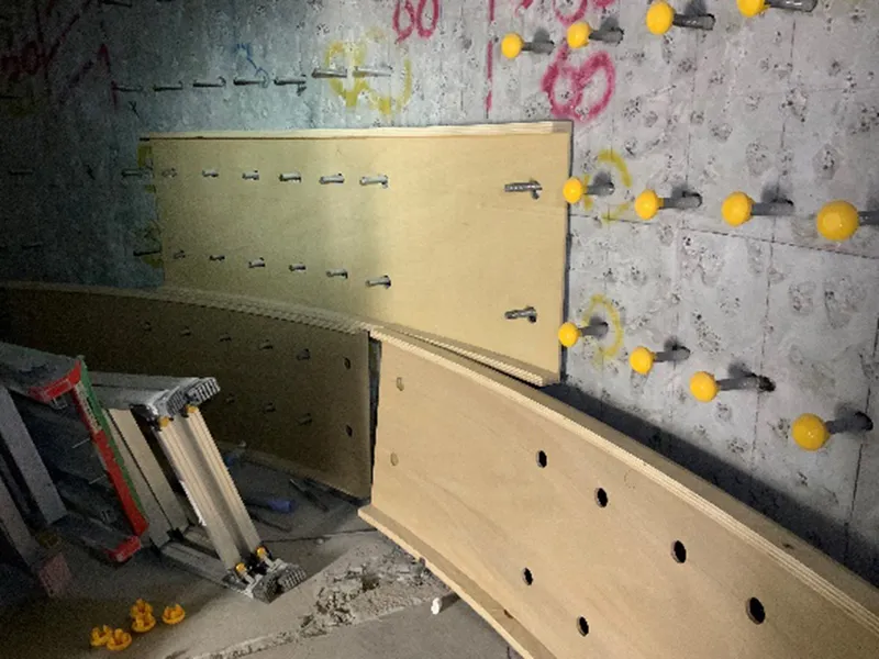 Plywood panel installation against a concrete wall marked with yellow sensors and graffiti during construction