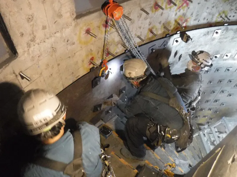Overhead view of workers installing metallic ceiling panels with chain hoist and temporary lighting