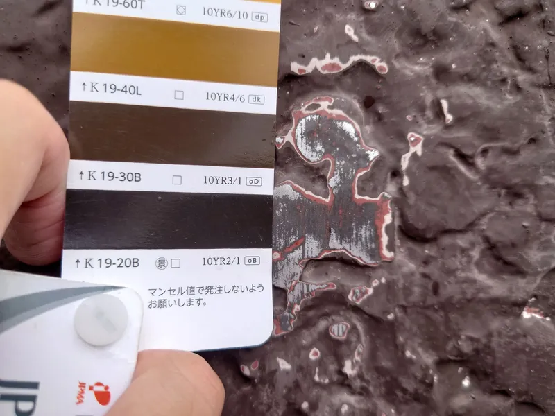 Hand holding color sample card against dark textured concrete surface during material selection