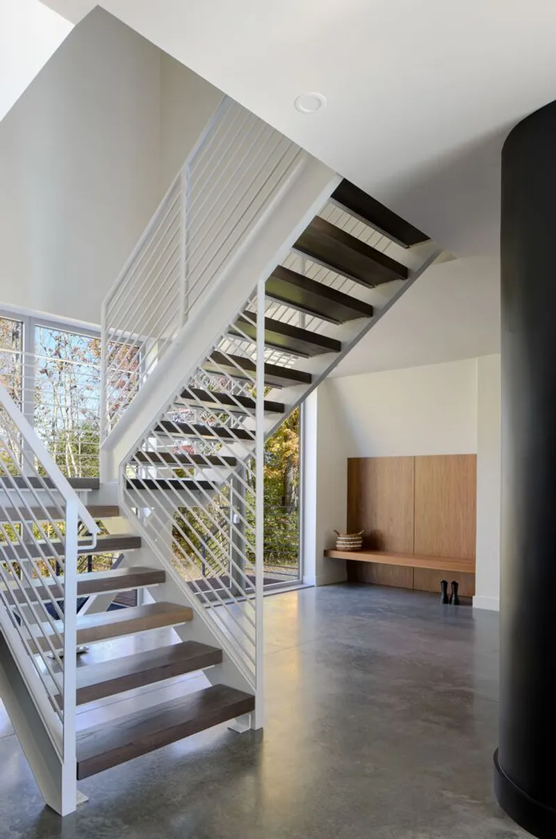 Open-tread staircase with white cable railings and dark treads beside a floor-to-ceiling window
