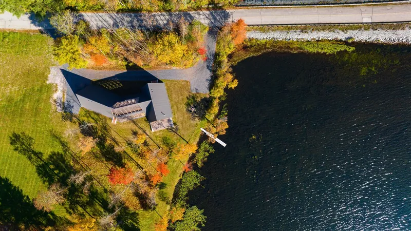 Drone view of the dark-roofed volumes on a narrow peninsula between lawn and lake in autumn