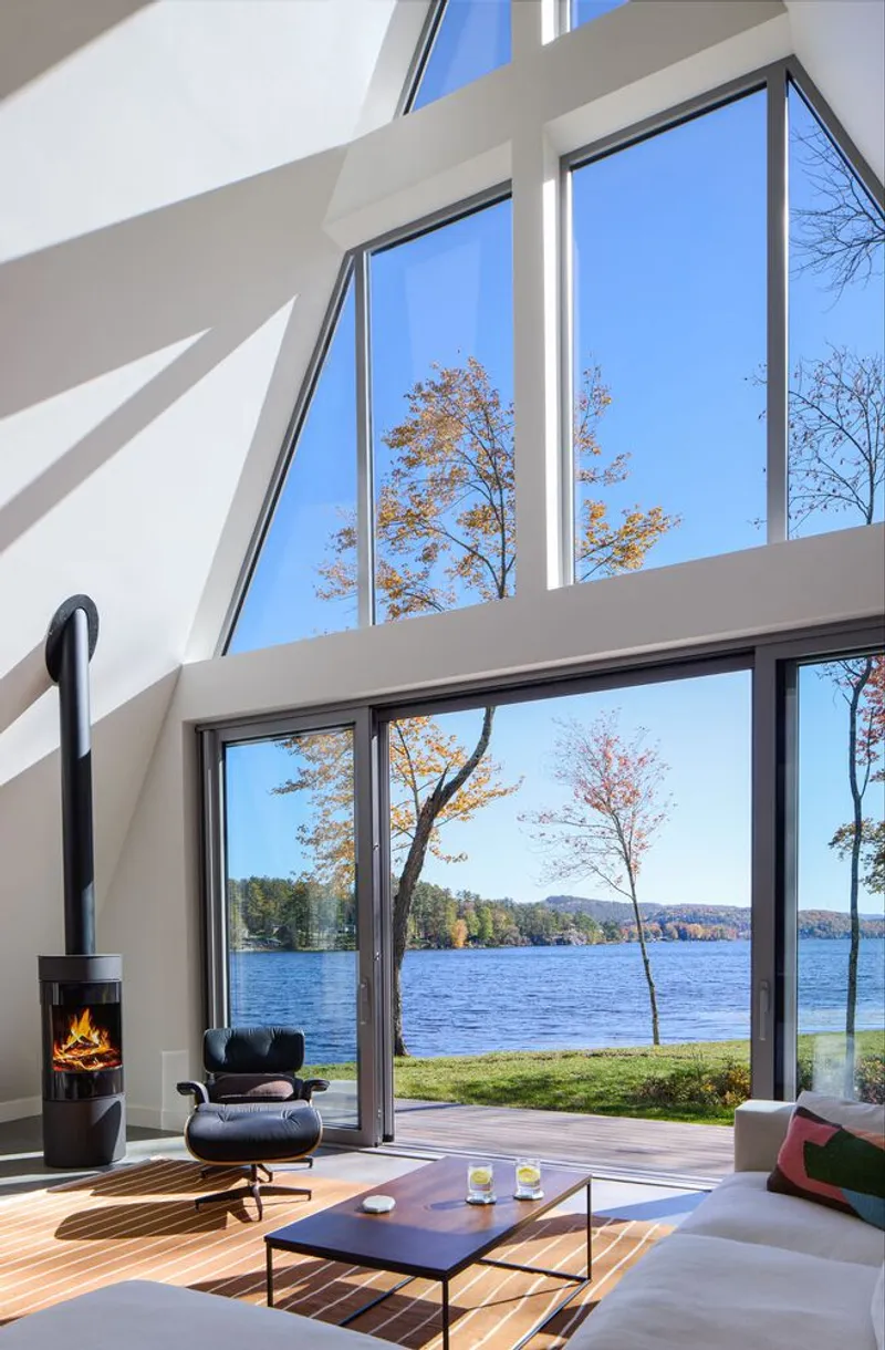 Double-height living room with floor-to-ceiling windows overlooking the lake and a wood-burning stove