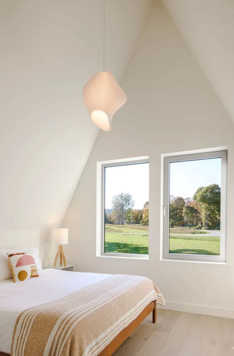 Bedroom with vaulted ceiling, twin casement windows and a pendant light in soft afternoon glow