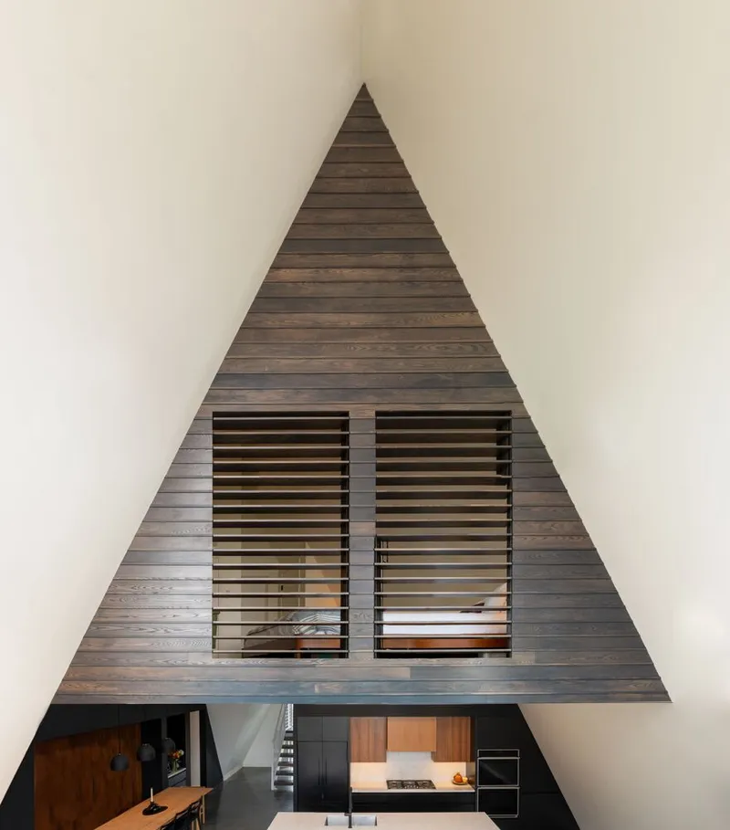 Triangular timber-clad wall with two horizontal louvered windows above an open living area