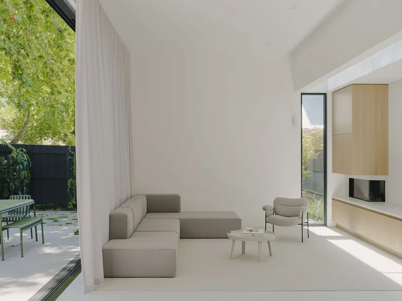Double-height living space with floor-to-ceiling curtains and glazing opening to a paved courtyard beyond