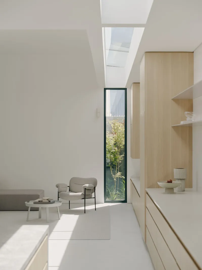 Interior view toward a narrow vertical window with skylight above casting sunlight across pale floors