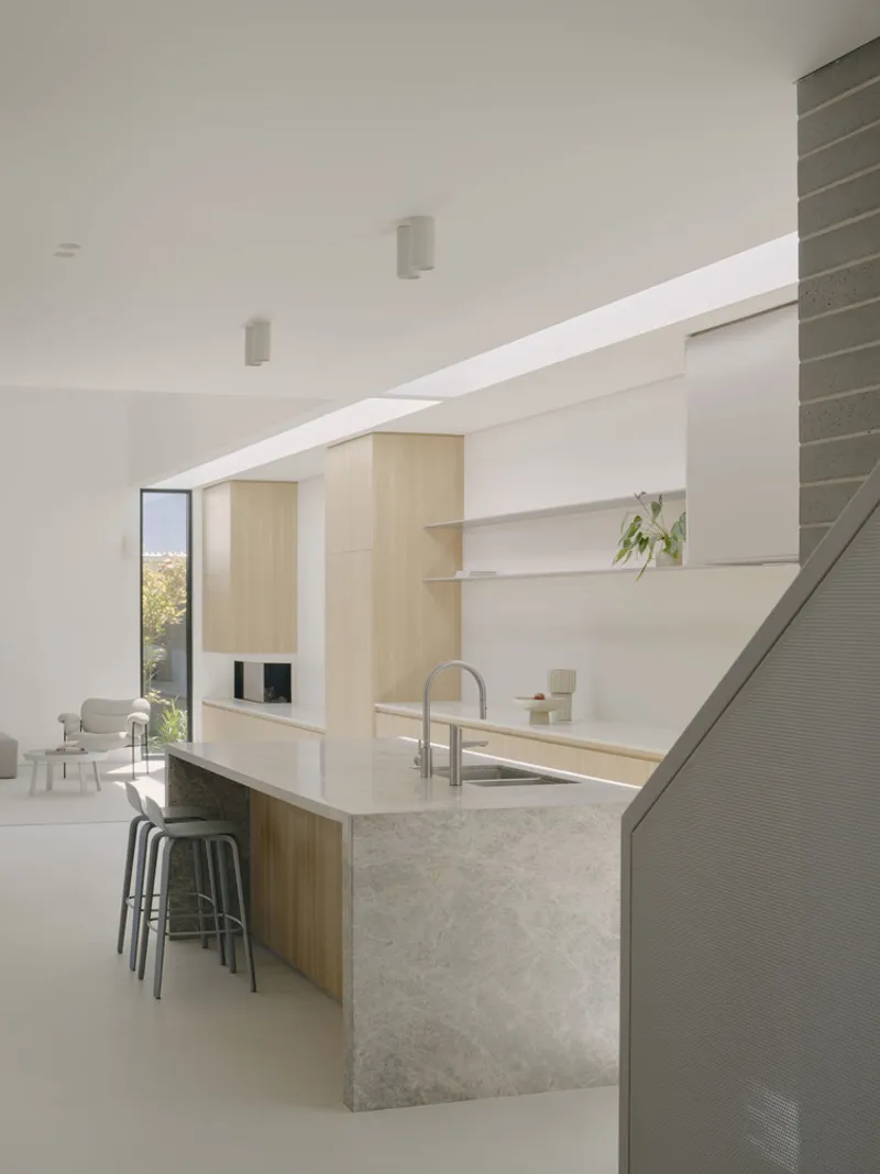 Kitchen island with terrazzo counter beneath angled skylight and pale timber cabinetry along the wall