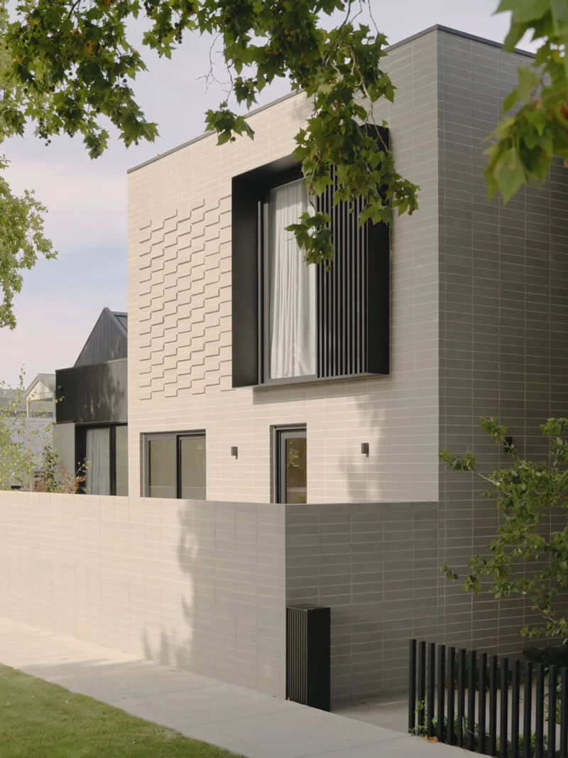Street view of tiered facade with textured brickwork under overhanging tree branches