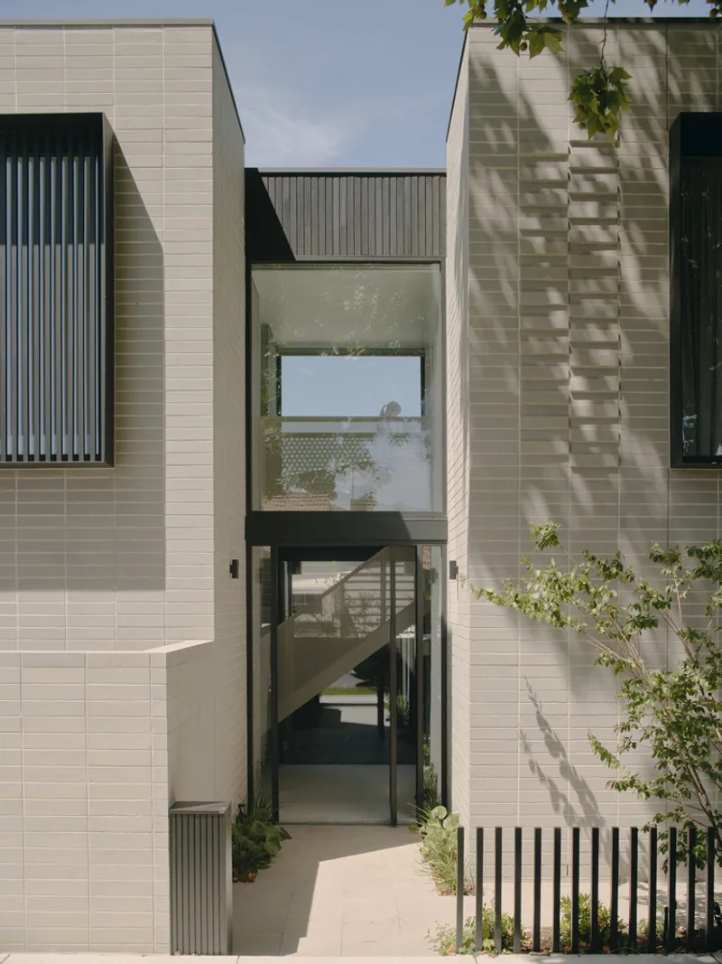 Entry courtyard with glazed doorway framed by pale brick walls and vertical black screening