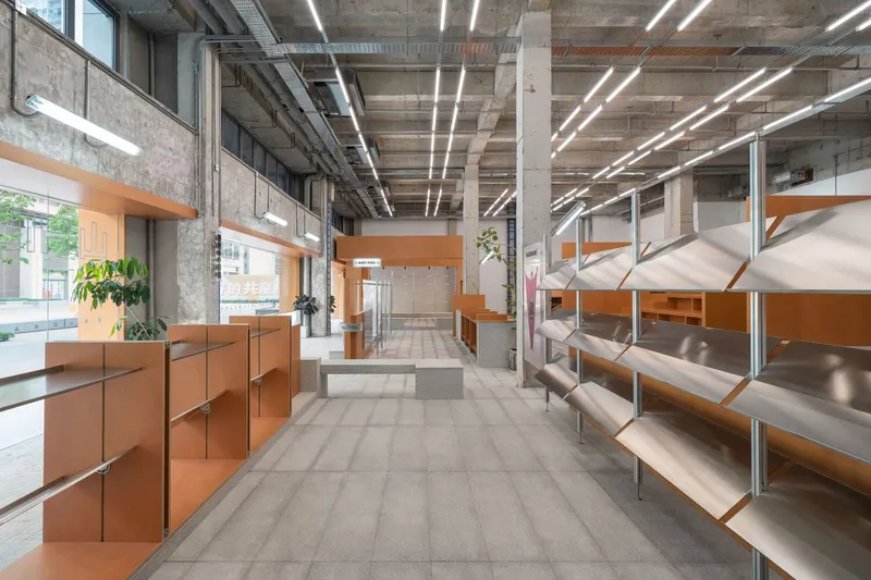 Interior view of retail space with exposed concrete ceiling, linear lighting, orange display units and metal shelving