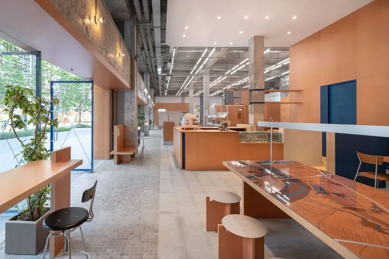 Orange service counter with transparent acrylic shelving under exposed concrete structure with potted plants