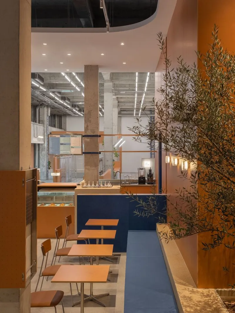Seating area with navy blue banquette, orange tables and olive tree adjacent to cafe counter