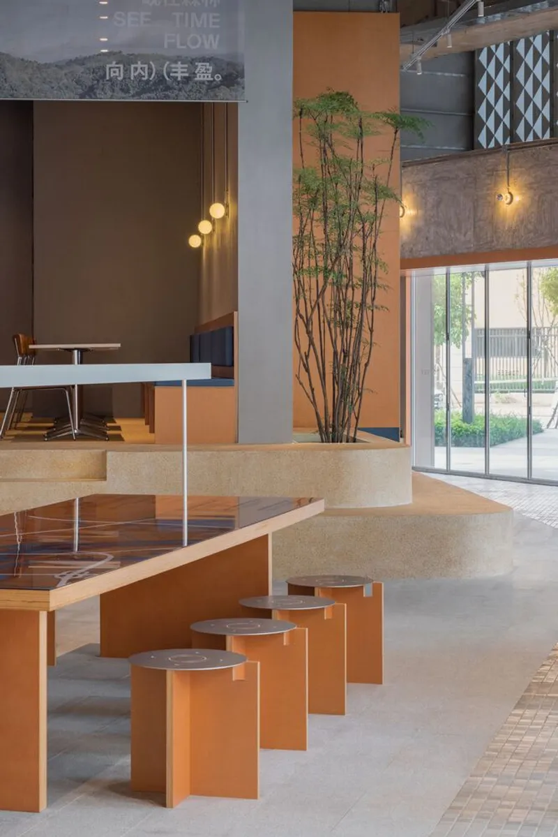 Orange steel communal table with round stools beside planter with tall bamboo and pendant lights