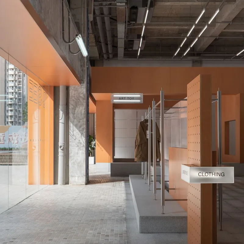 Corridor with metal clothing racks and orange panels beneath exposed mechanical ducts in afternoon sunlight