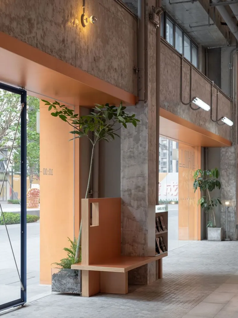Orange bench with planters wrapped around concrete column near glazed entrance with view to exterior