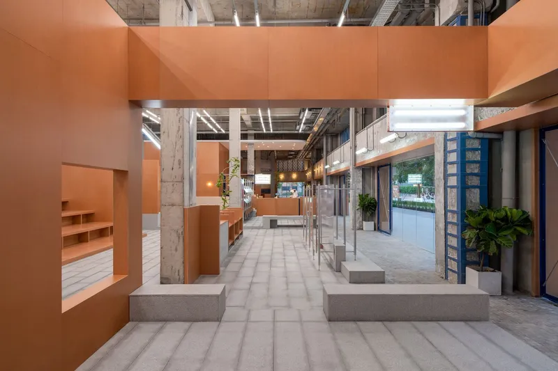 Orange partition volumes framing concrete benches along the tile floor with potted plants visible through glazing