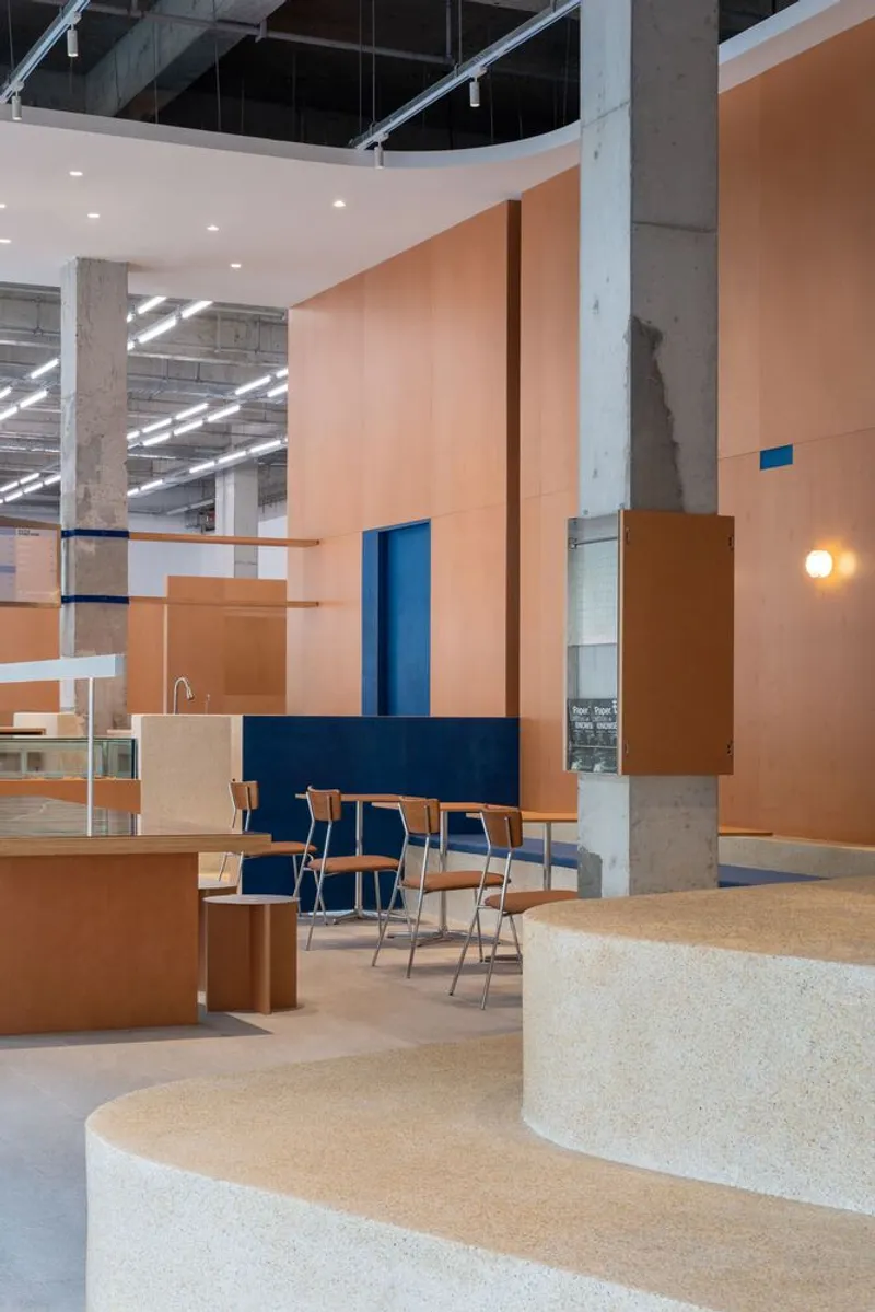 Seating area with blue upholstered chairs at timber table on curved terrazzo step beside concrete column