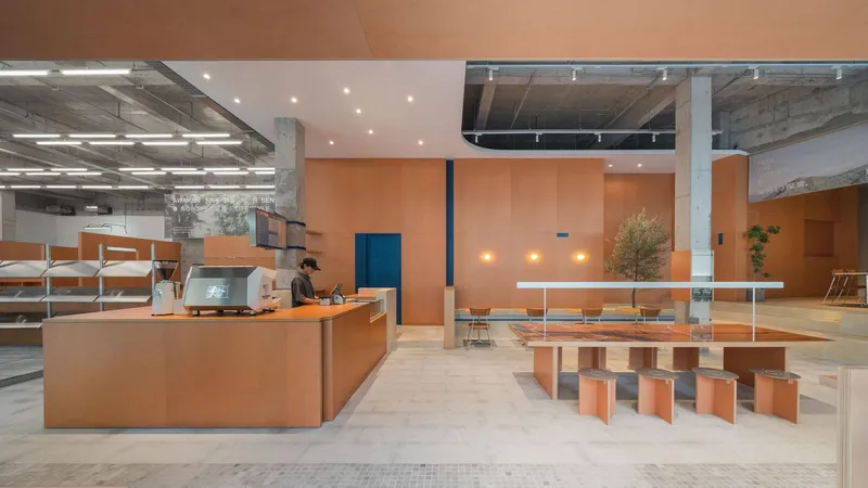 Orange service counter with staff member and seating table beneath peach-toned ceiling with recessed lighting