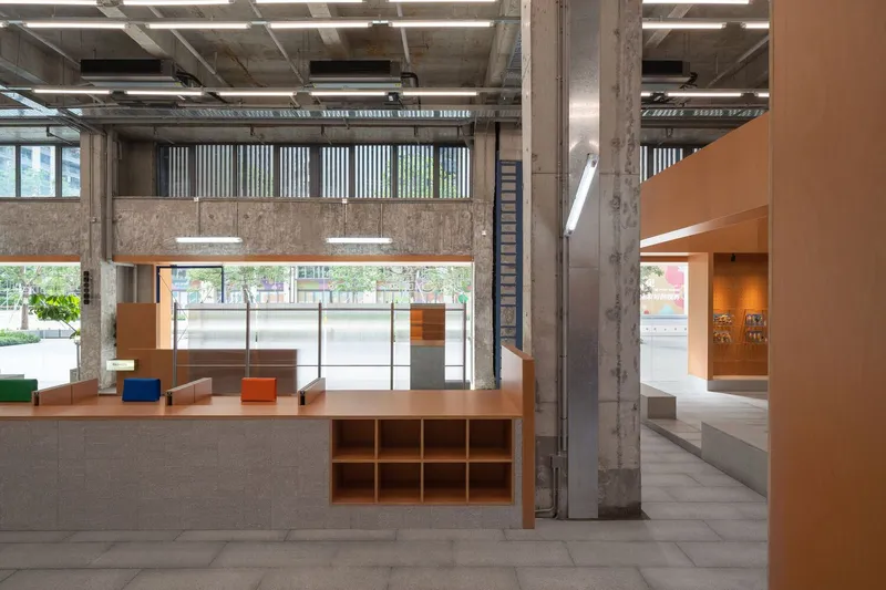 Double-height lobby with exposed concrete columns, industrial ceiling and timber display tables facing glazed entrance