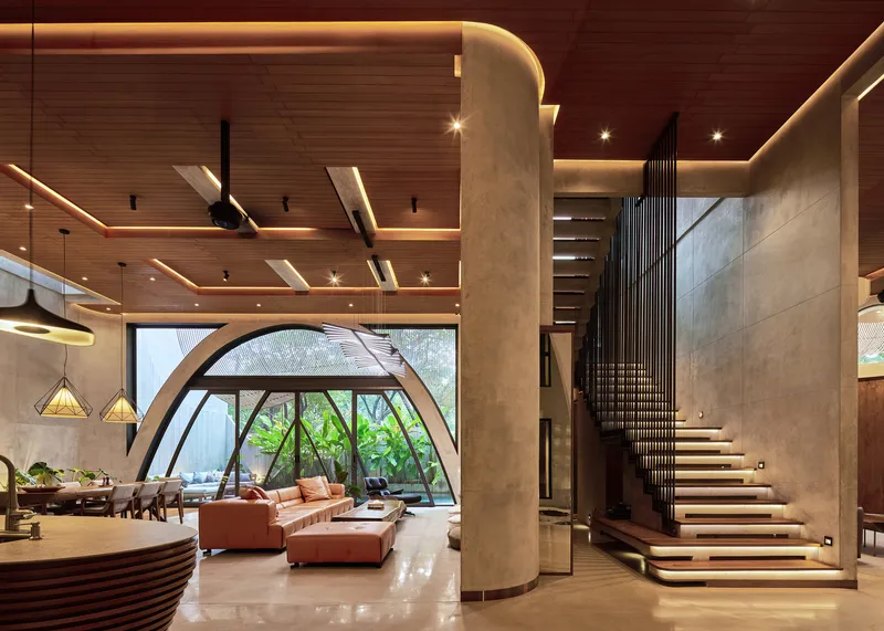 Double-height living space with arched window wall and floating timber staircase beside a cylindrical concrete column