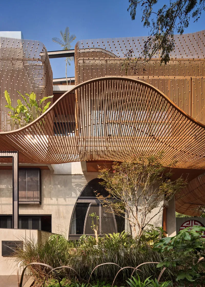 Curving timber slat canopy above concrete arched windows framed by garden beds and tree branches