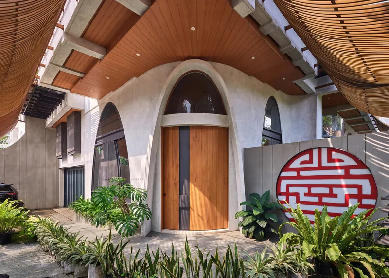 Arched timber entry door under curved concrete portal with circular red geometric screen in courtyard garden
