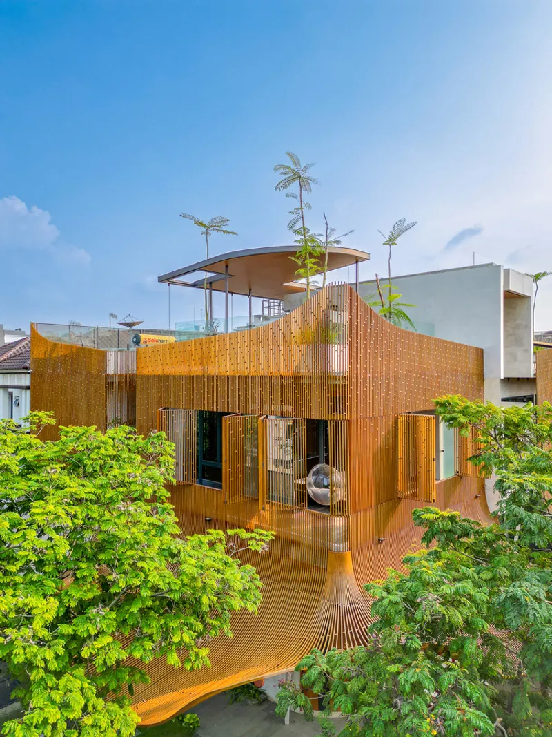 Curved perforated metal facade with operable panels surrounded by lush tropical vegetation under blue sky