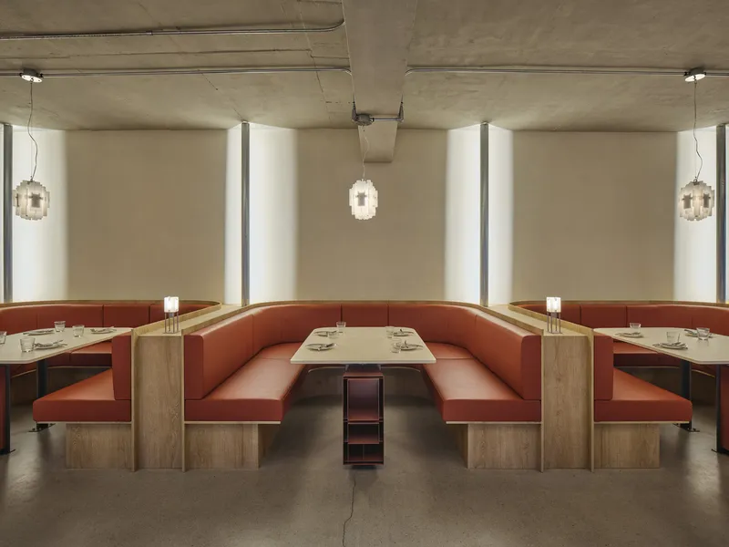 Dining area with terracotta banquette seating, timber tables, and pendant lights under an exposed concrete ceiling