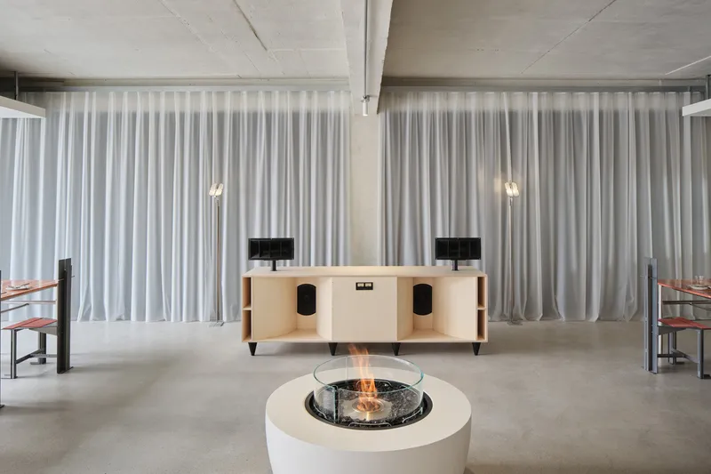 Lounge space with central circular fireplace, credenza, and floor-to-ceiling sheer curtains filtering natural light