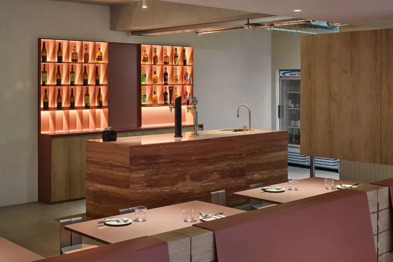 Bar area with backlit orange shelving, timber counter and pink upholstered banquettes
