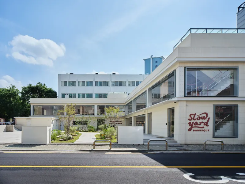 Street view of white facade with planted terrace and neighboring buildings under clear sky