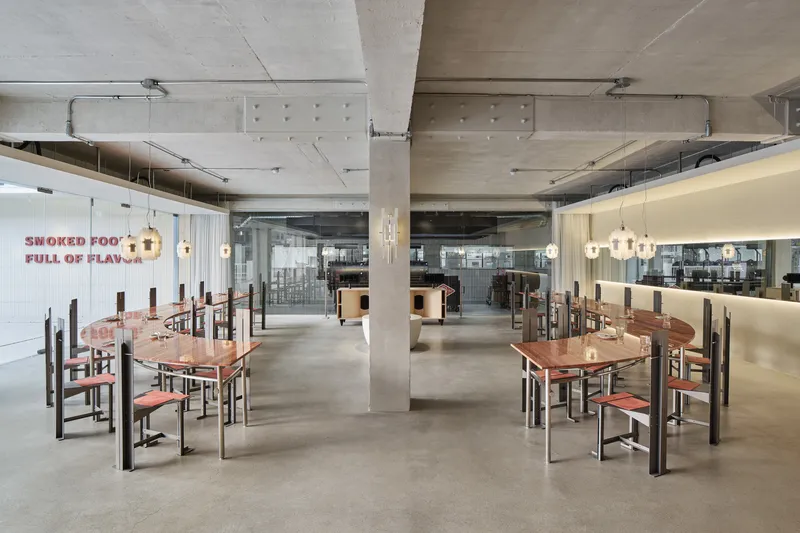 Restaurant dining room with exposed concrete ceiling, timber tables and pendant lights over polished concrete floors