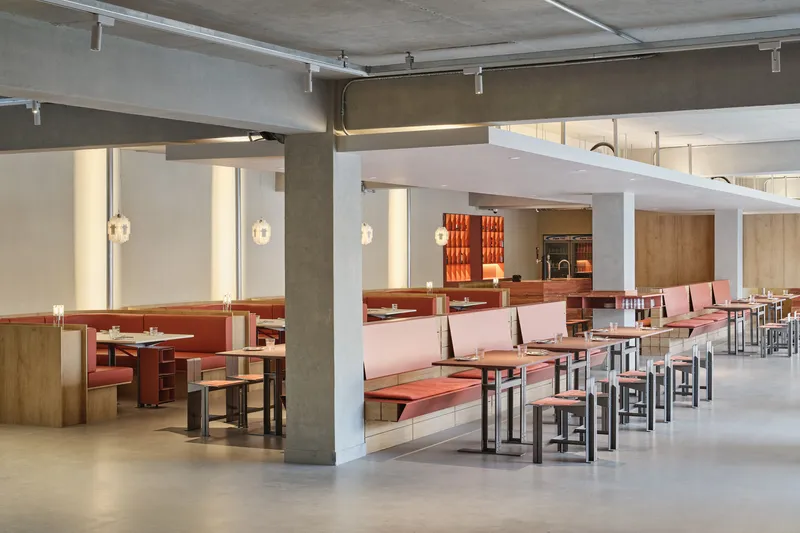 Dining space showing concrete columns, white framing elements and rows of pink banquette seating