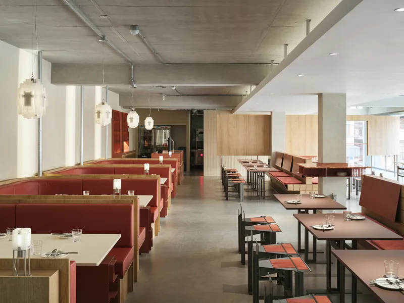 Long view through dining room showing exposed ceiling ducts, concrete beams and red upholstered booth seating