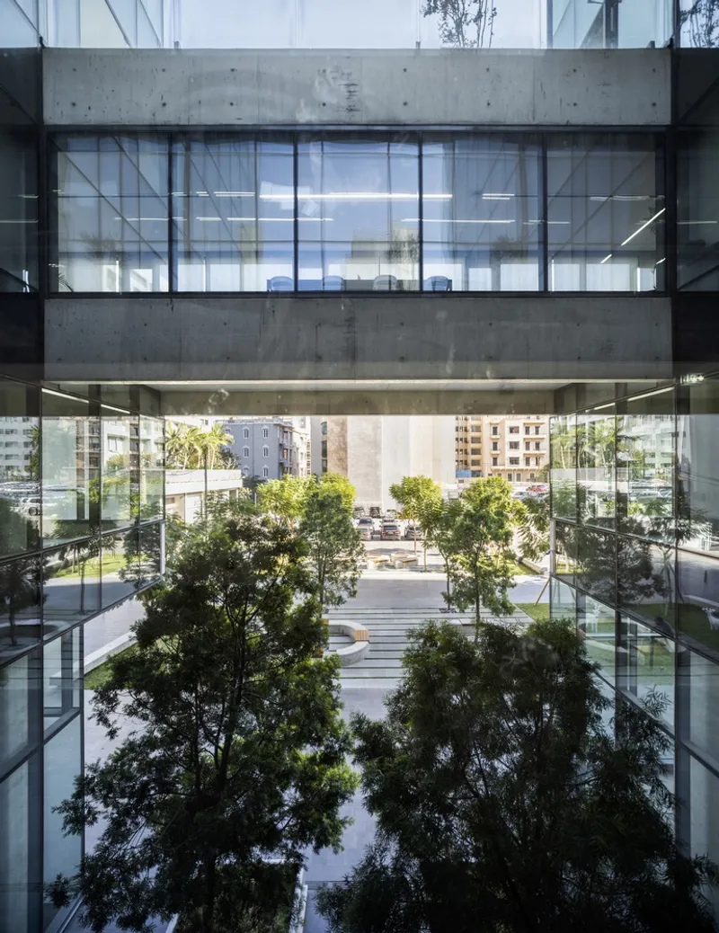 View through glass lobby showing concrete beams framing trees in the courtyard beyond