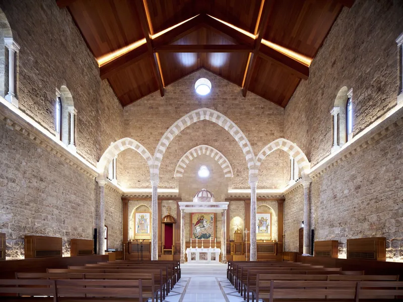 Altar wall with striped stone arches, timber ceiling and central oculus above wooden pews