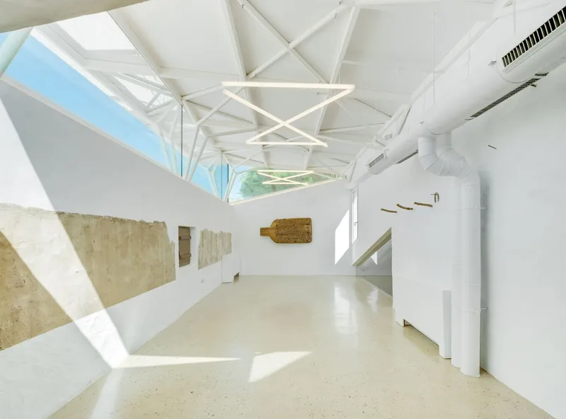 Gallery space with exposed white structural trusses and clerestory windows casting daylight across polished concrete floors