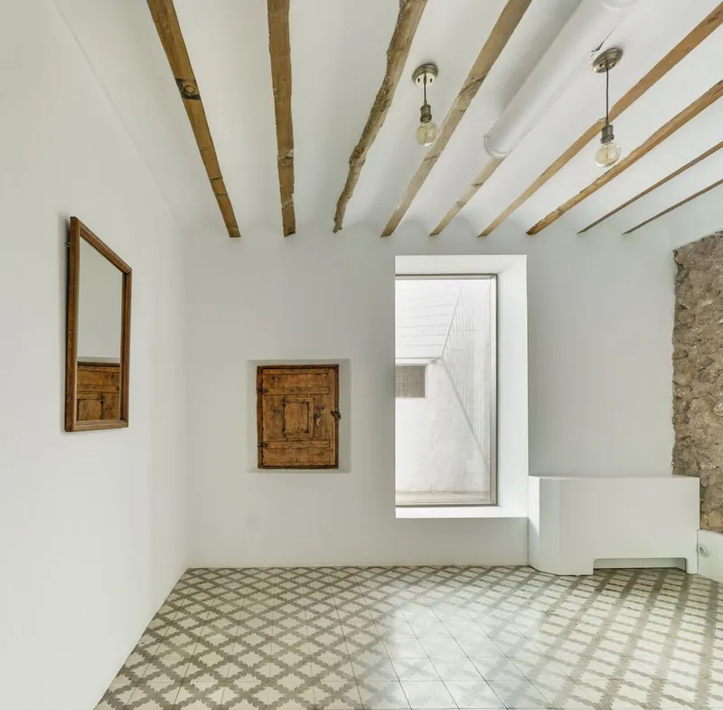 Room with exposed timber ceiling beams and geometric patterned floor tiles leading to a framed interior opening