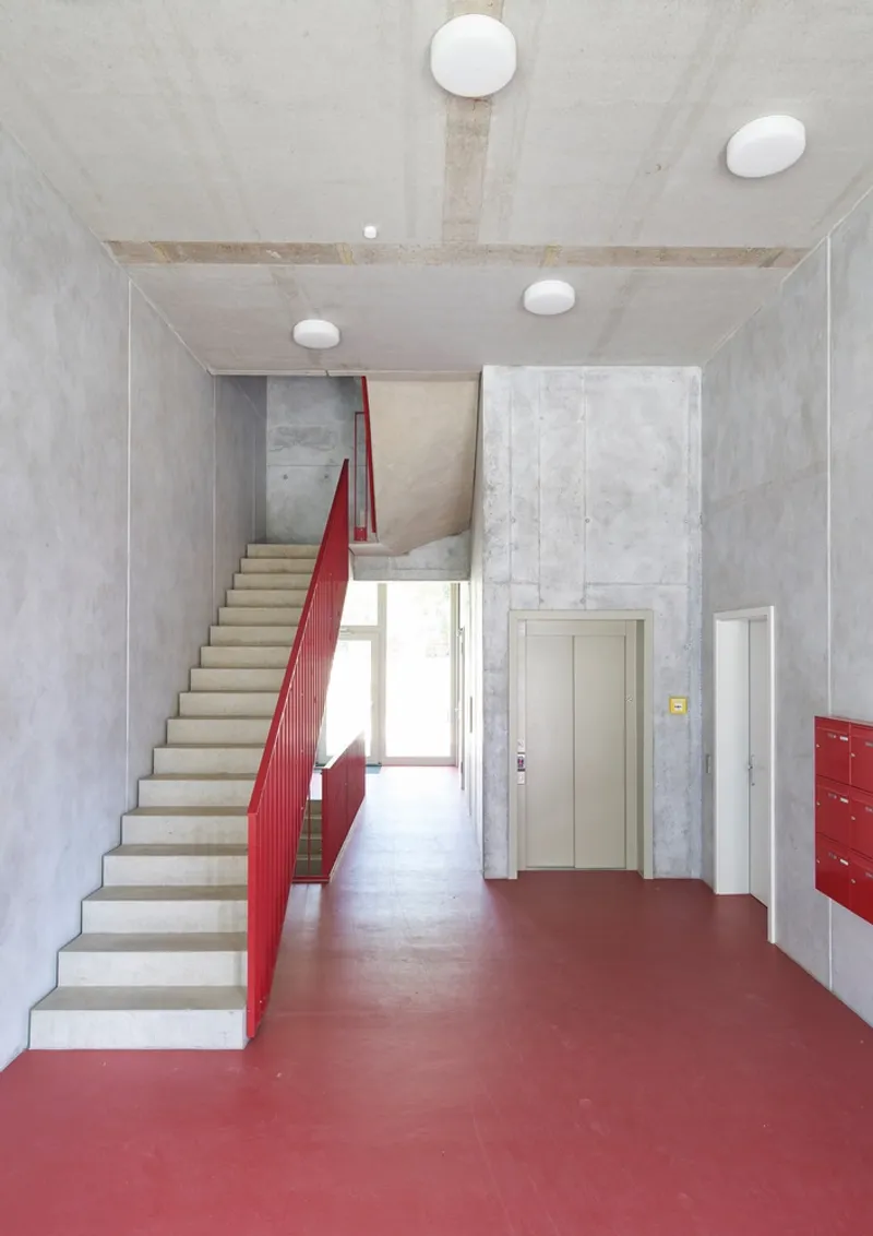 Concrete staircase with red metal balustrade rising from the pink resin floor of the entrance hall