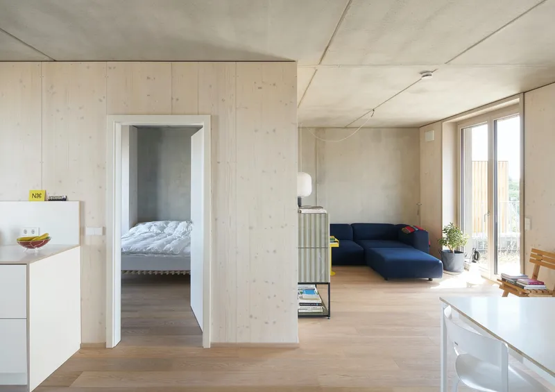 Plywood partition wall separating the living room from the bedroom doorway with concrete ceiling above