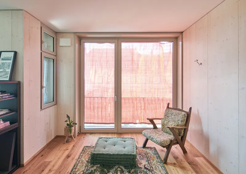 Small sitting room with plywood walls and glazed balcony doors behind pink mesh curtains