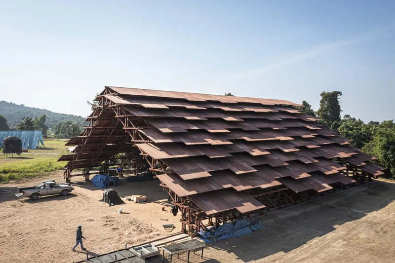 Large timber-framed pavilion with layered copper roof canopy on an open construction site