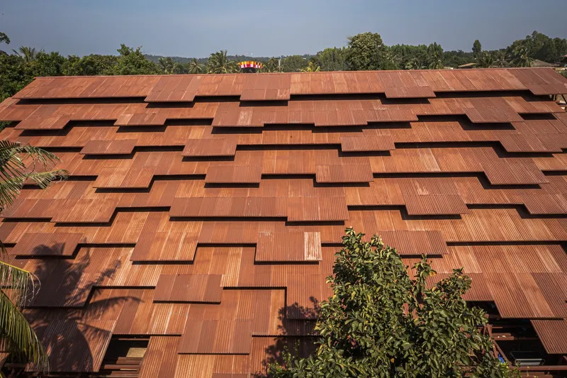 Copper shingle roof with offset openings creating shadow patterns beside a treetop