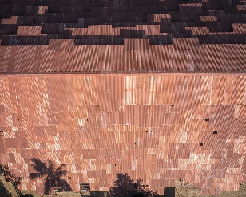 Close-up of the weathered terracotta brick facade with vertical striations and plant shadows