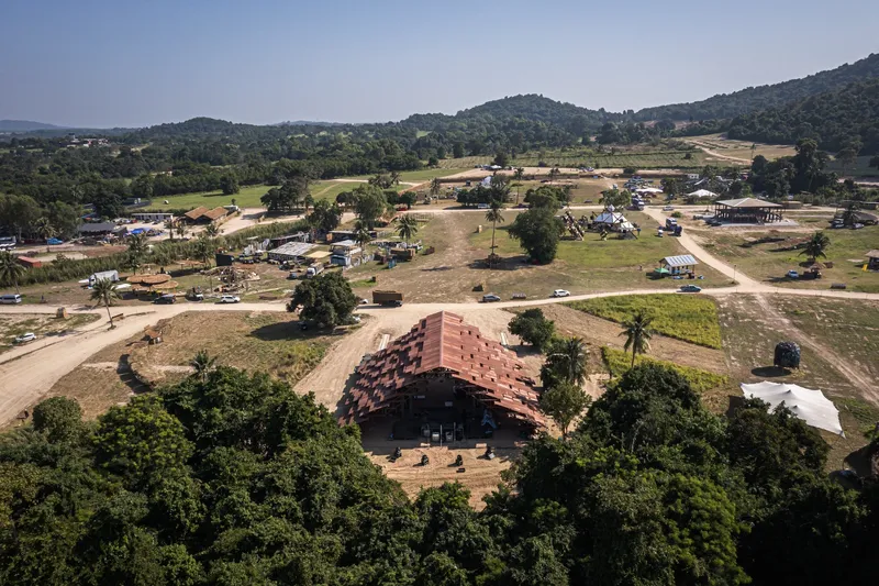 Aerial view of the stepped terracotta brick pavilion surrounded by palms and rural landscape